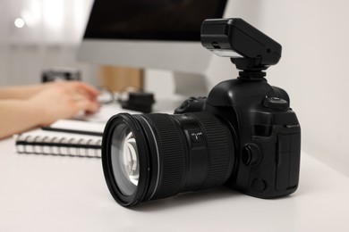 Photographer working on computer at white table with camera indoors, closeup