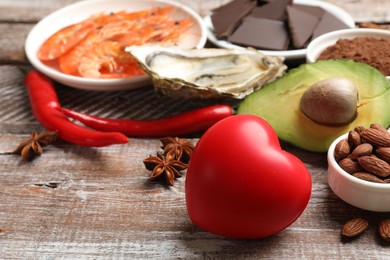 Photo of Natural aphrodisiac. Different food products and heart model on wooden table, closeup