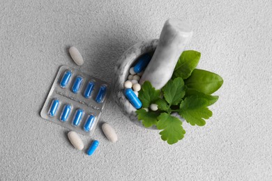 Photo of Marble mortar with fresh green herbs and pills on white table, flat lay