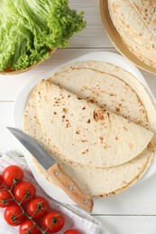 Tasty homemade tortillas, tomatoes, lettuce and knife on white wooden table, top view