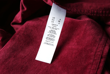 Photo of Clothing label with size and content information on red garment, closeup