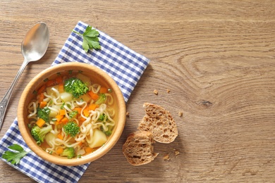 Photo of Bowl of fresh homemade vegetable soup served on wooden table, flat lay. Space for text