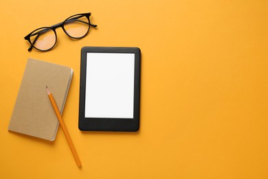 Modern e-book reader, glasses, notebook and pencil on orange background, flat lay. Space for text