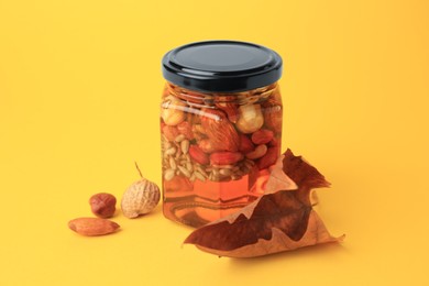 Photo of Different nuts with honey in jar and dry leaf on yellow background