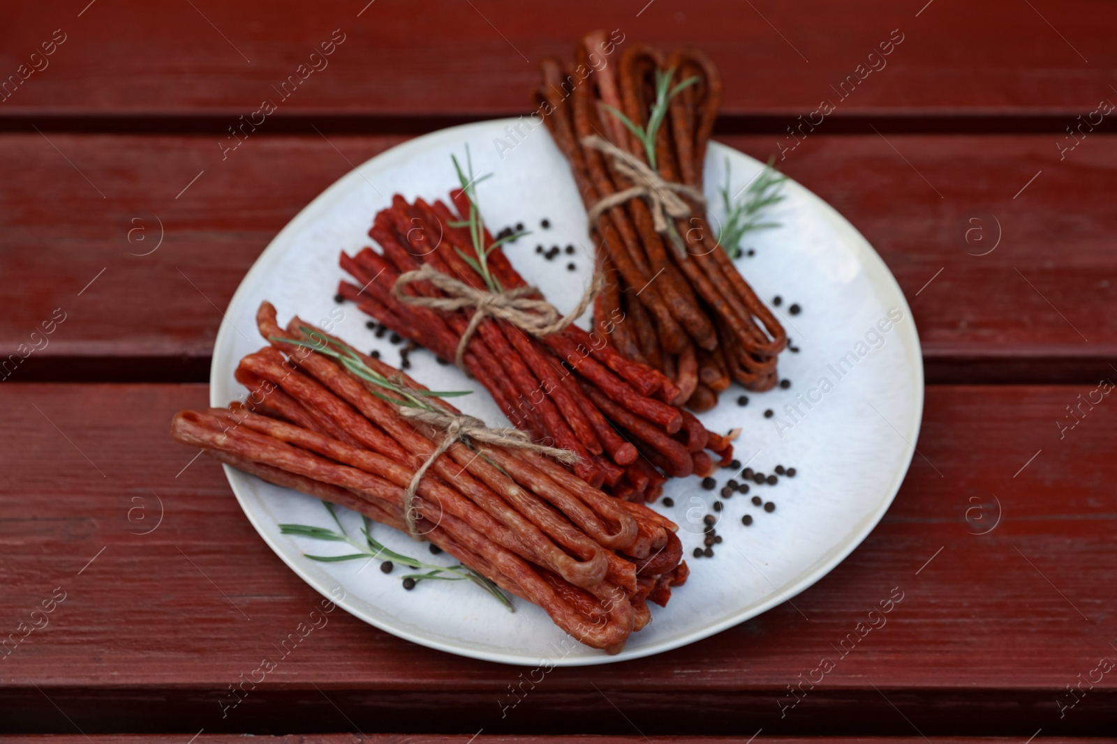 Photo of Tasty dry cured sausages (kabanosy) and spices on wooden table