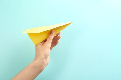 Woman holding paper plane on light blue background, closeup. Space for text