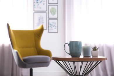 Side table with cup and succulent near comfortable armchair in room. Stylish interior elements