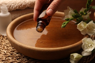 Photo of Woman dripping essential oil into bowl at table, closeup. Aromatherapy treatment