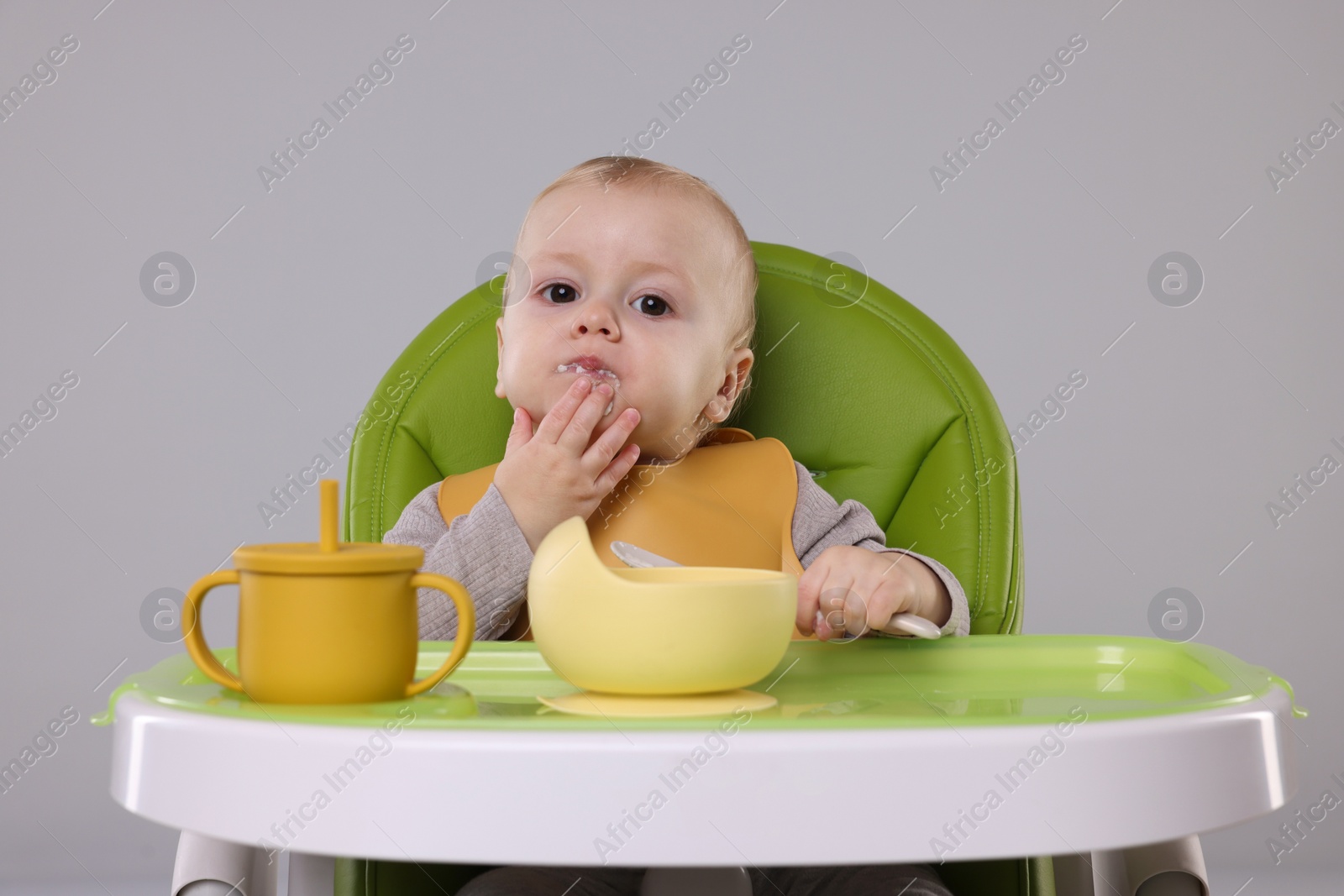 Photo of Cute little baby eating healthy food in high chair on gray background