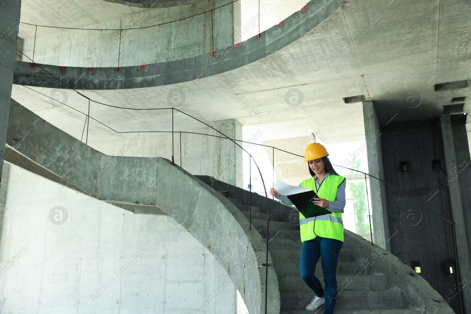 Photo of Professional engineer in safety equipment with clipboard at construction site. Space for text