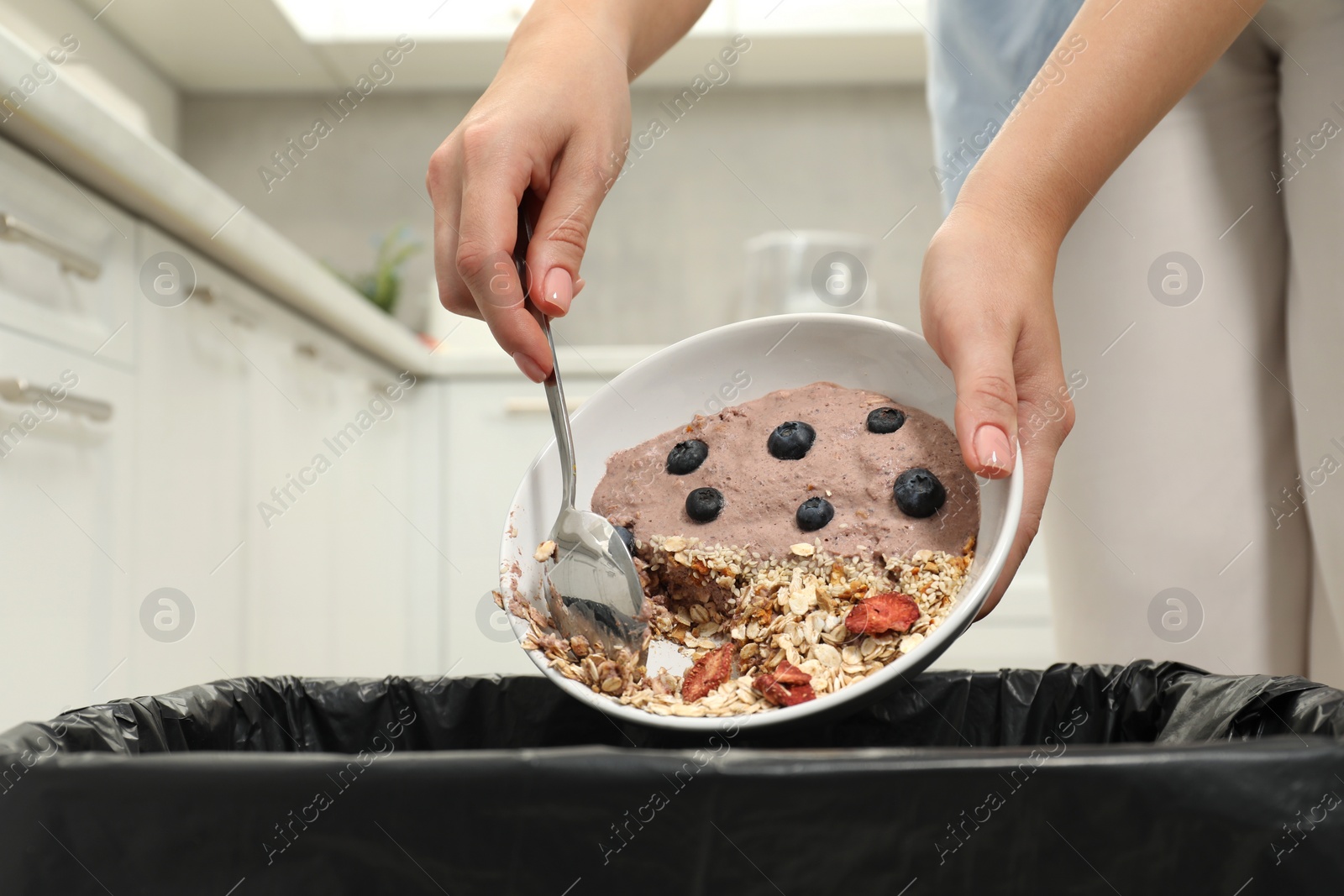 Photo of Woman throwing oatmeal with berries into bin indoors, closeup