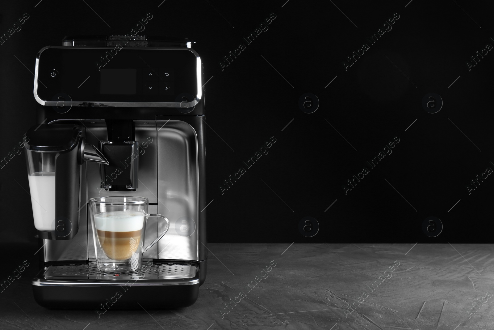 Photo of Modern coffee machine with glass cup of latte on grey table against black background. Space for text