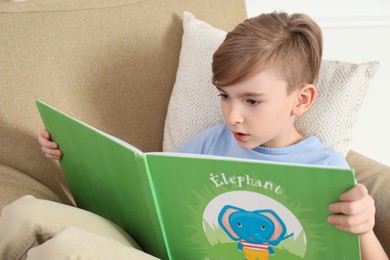 Little boy reading book in armchair at home