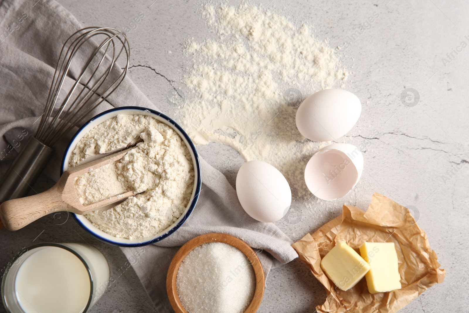 Photo of Different ingredients for dough and whisk on light textured table, flat lay