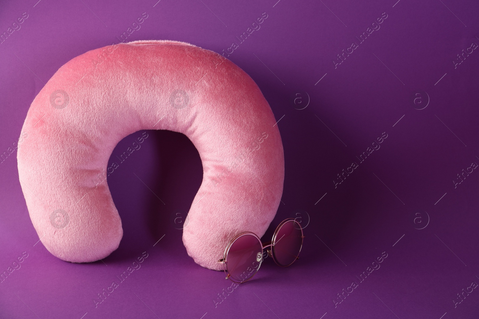 Photo of Pink travel pillow and sunglasses on violet background