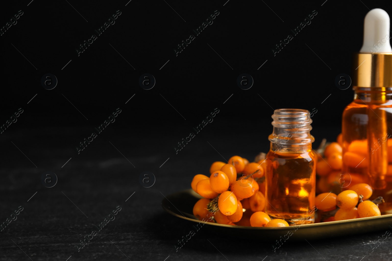 Photo of Ripe sea buckthorn and bottles of essential oil on black table. Space for text