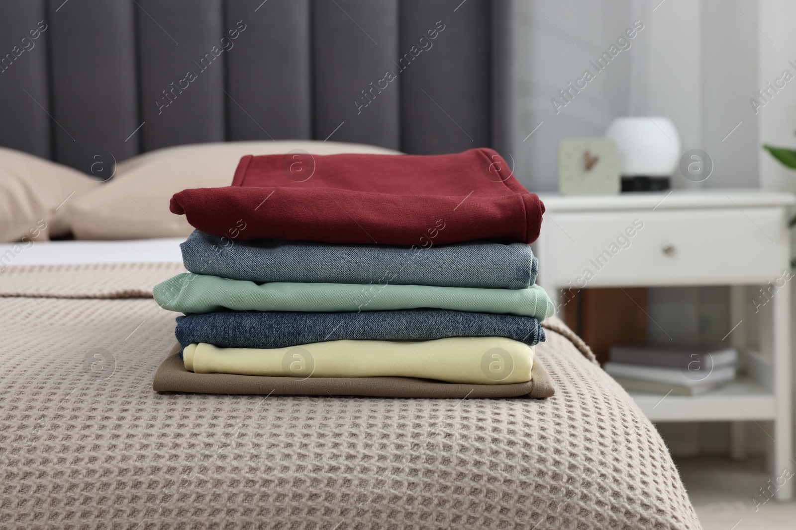 Photo of Stack of different folded clothes on bed at home