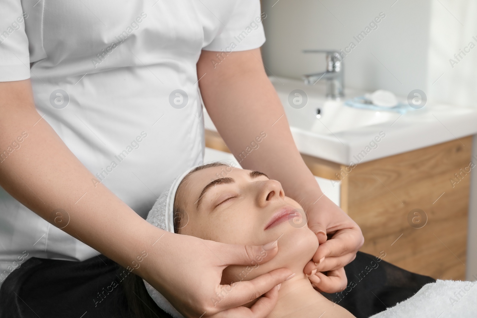 Photo of Cosmetologist making face massage to client in clinic, closeup