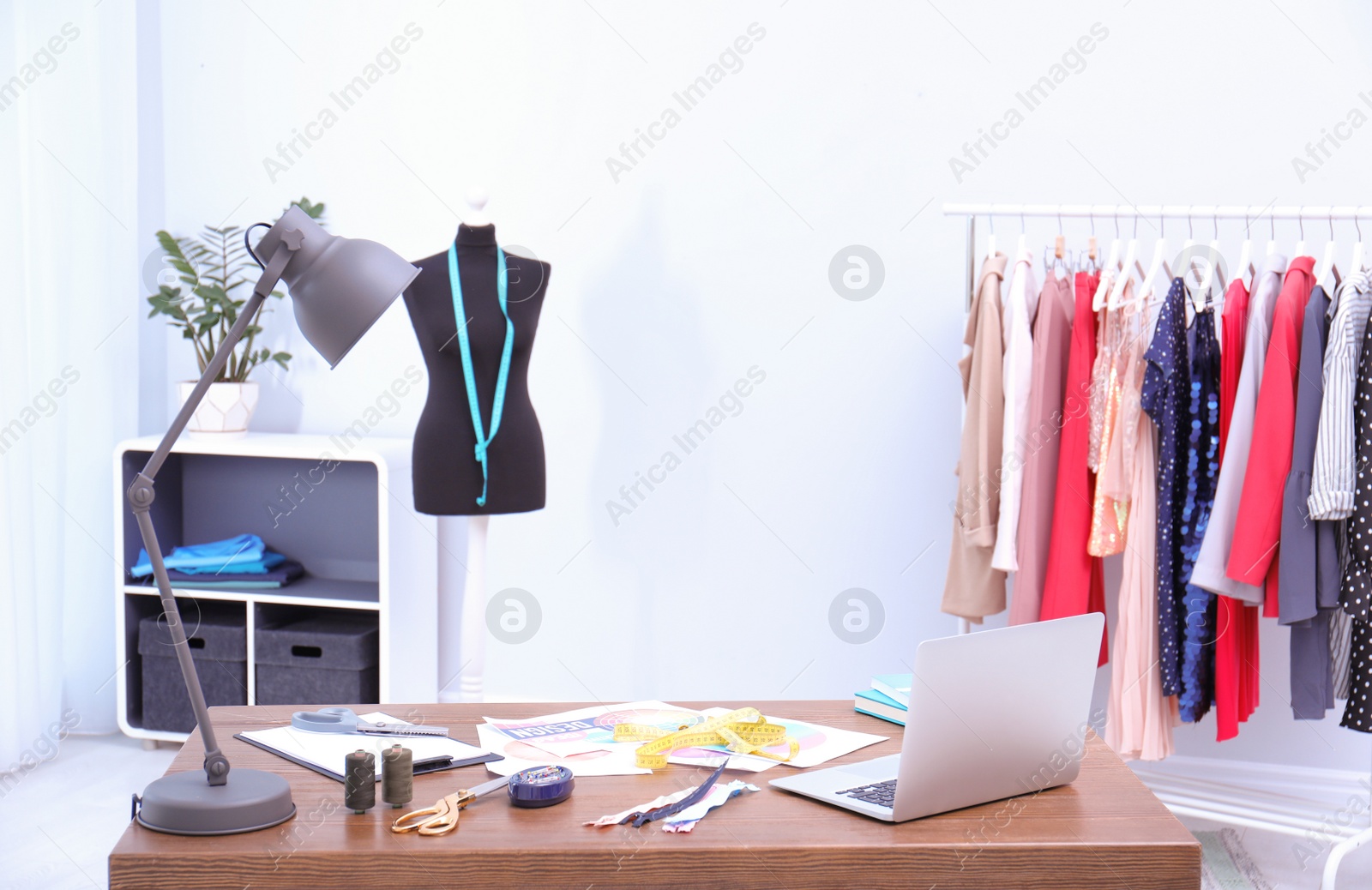 Photo of Stylist's workplace with comfortable desk and rack with clothes