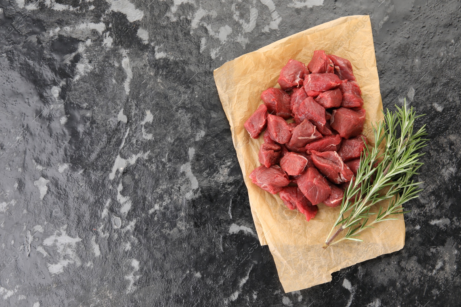 Photo of Pieces of raw beef meat and rosemary on grey textured table, top view. Space for text