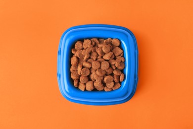 Photo of Dry pet food in feeding bowl on orange background, top view