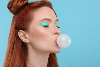 Photo of Beautiful woman with bright makeup and closed eyes blowing bubble gum on light blue background. Space for text