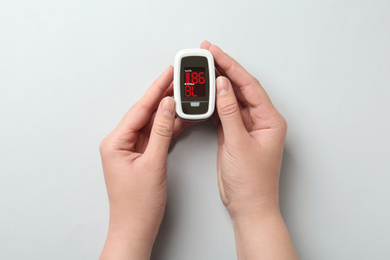 Woman holding fingertip pulse oximeter on white background, top view