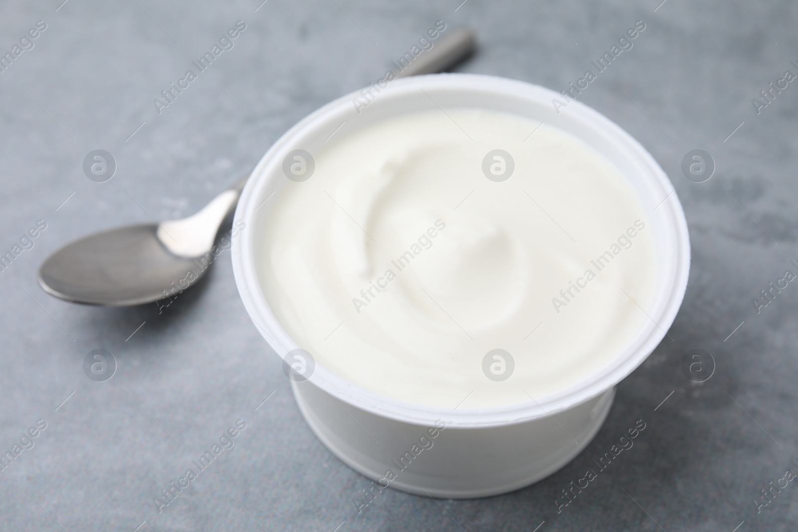 Photo of Delicious natural yogurt in plastic cup and spoon on grey table, closeup