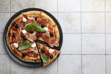 Tasty pizza with cured ham, olives, mozzarella cheese, sun-dried tomato and basil on light tiled table, top view. Space for text