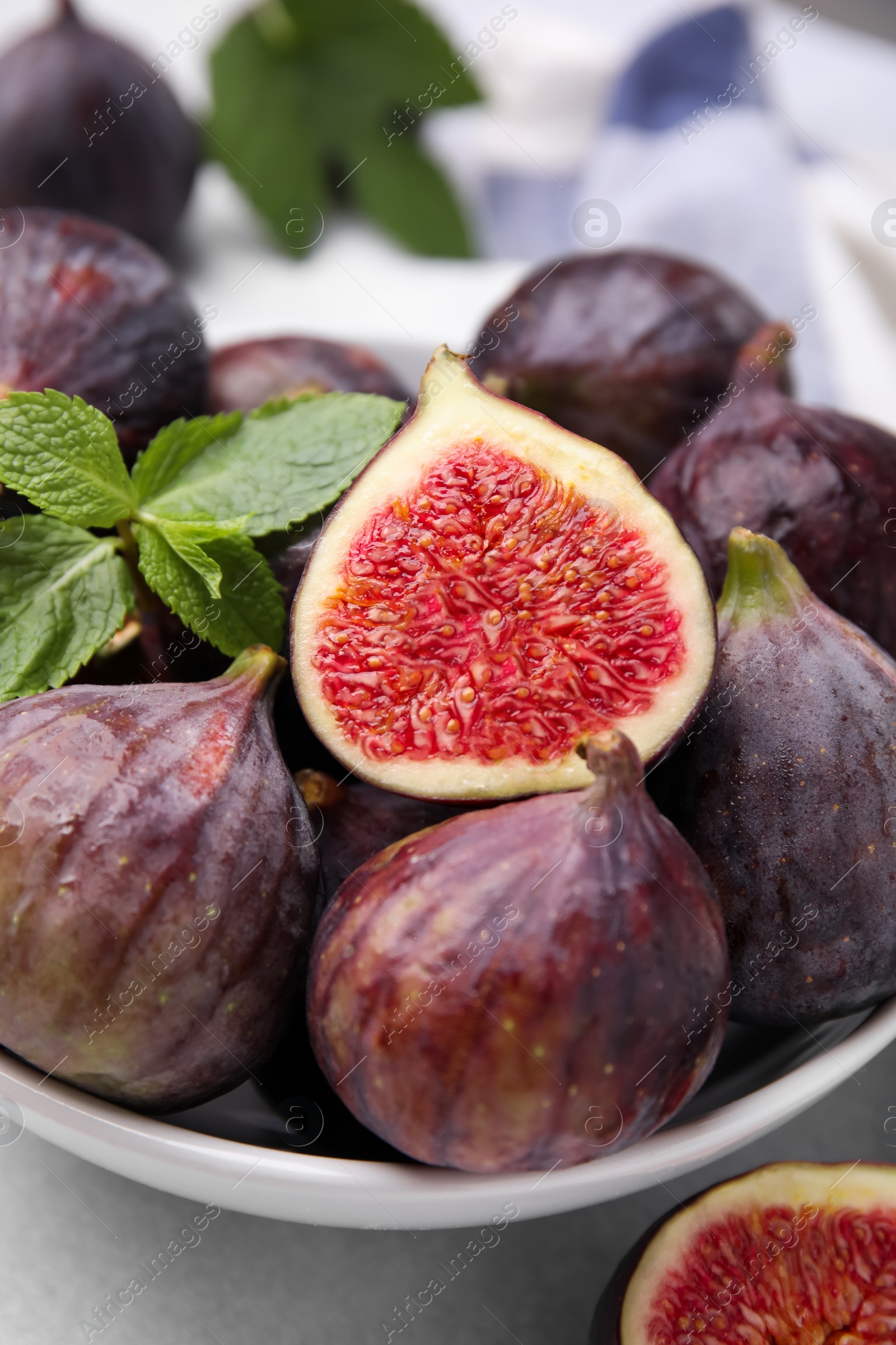 Photo of Bowl of tasty ripe figs and mint on light table, closeup