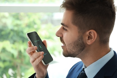 Photo of Young man using voice search on smartphone indoors