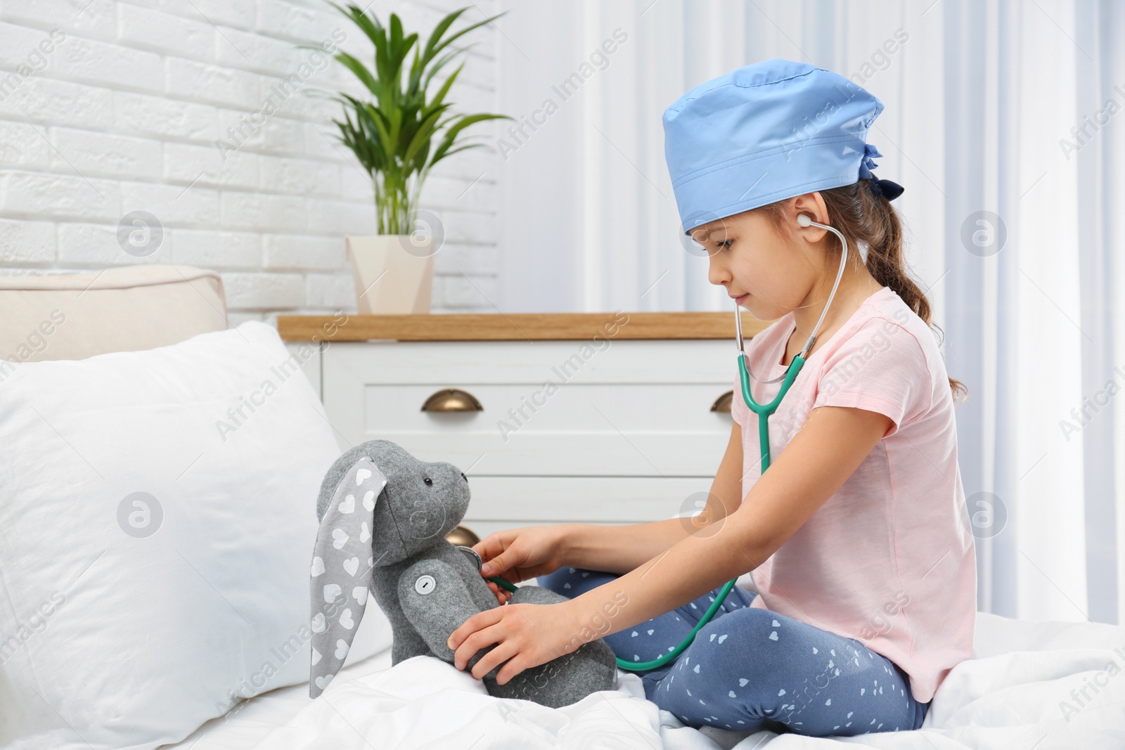 Photo of Cute child playing doctor with stuffed toy on bed in hospital ward