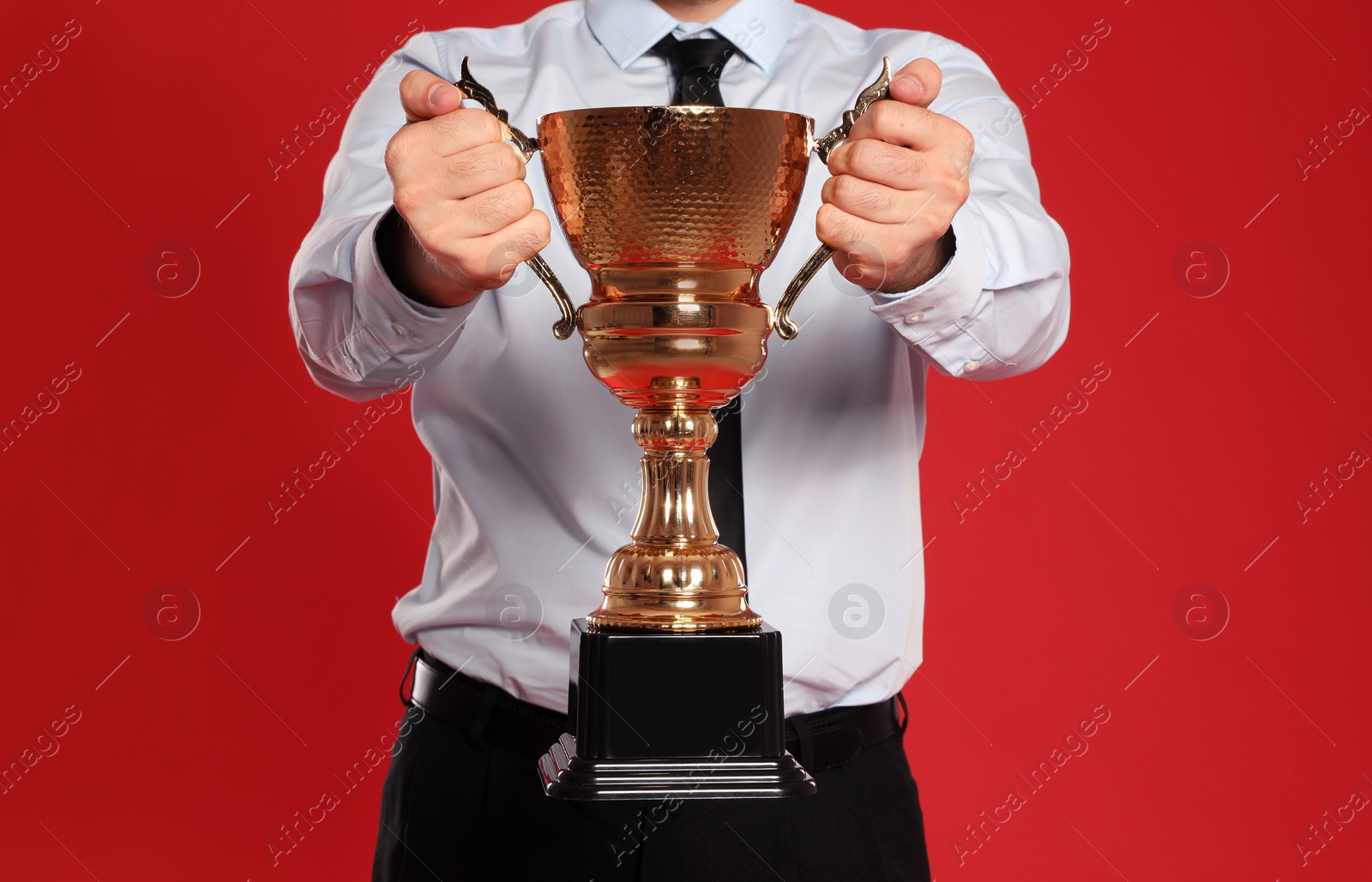 Photo of Young businessman with gold trophy cup on red background, closeup