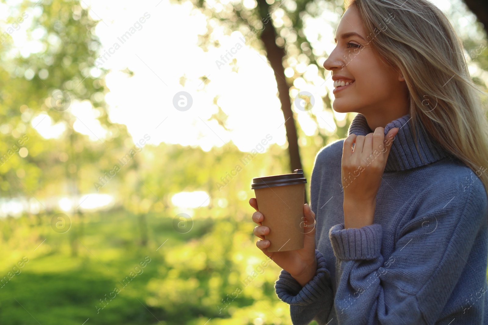 Photo of Beautiful young woman with coffee cup wearing stylish sweater in autumn park