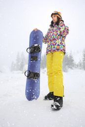 Young woman with snowboard wearing winter sport clothes outdoors, low angle view