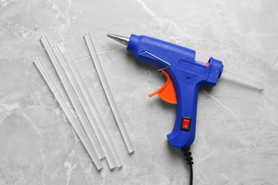 Photo of Blue glue gun and sticks on light grey marble table, flat lay