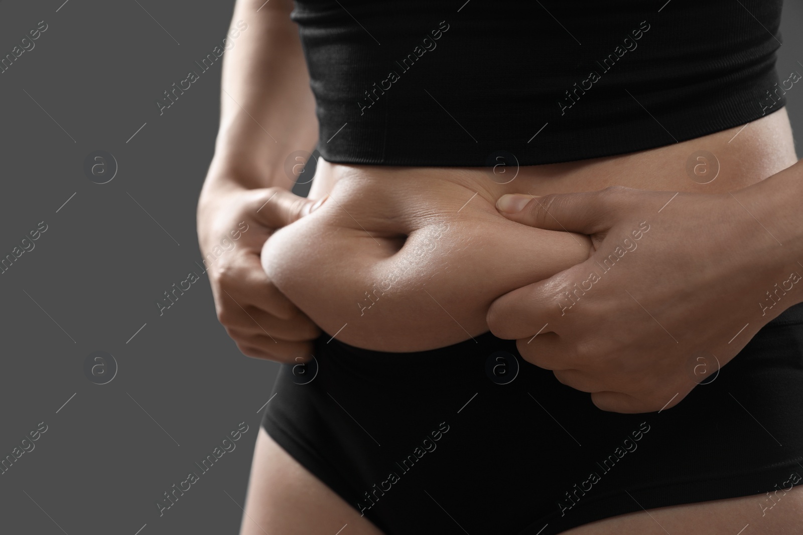 Photo of Woman touching belly fat on grey background, closeup. Overweight problem