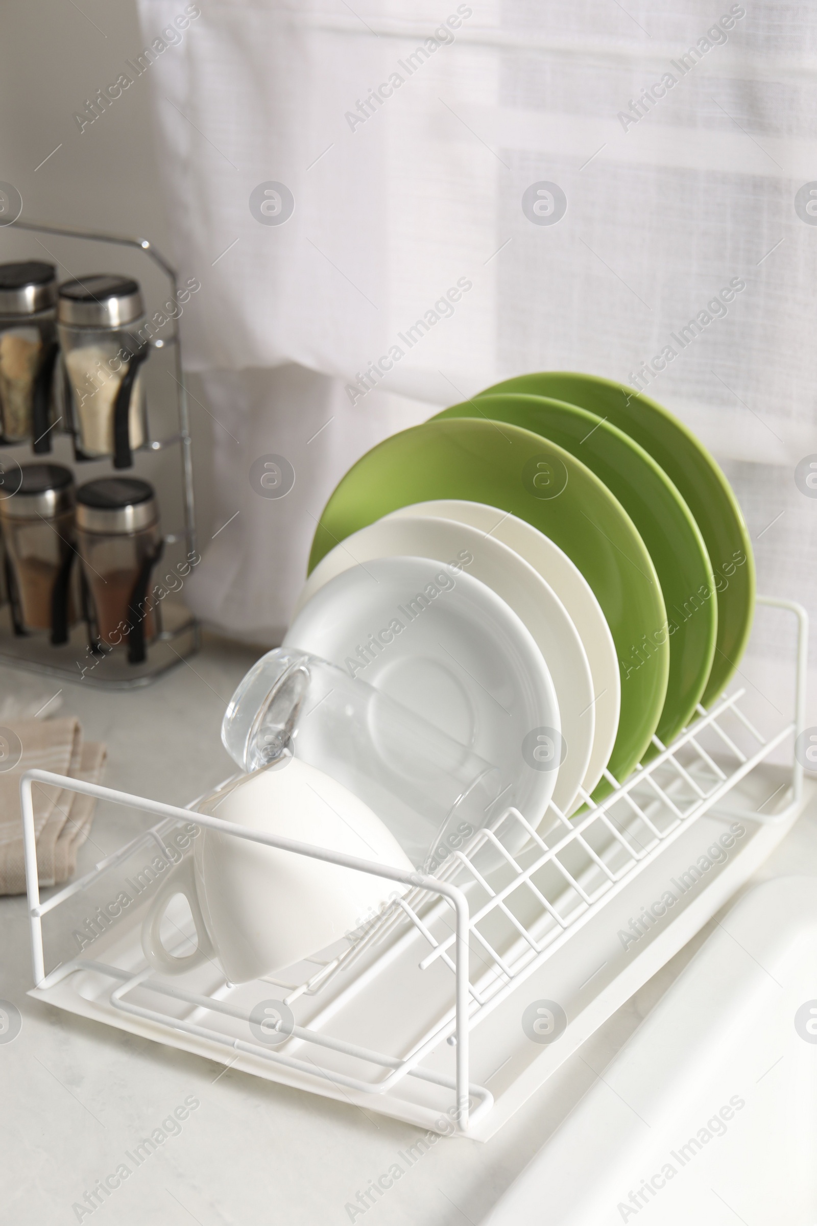 Photo of Drainer with different clean dishware, glass and cup on white table indoors