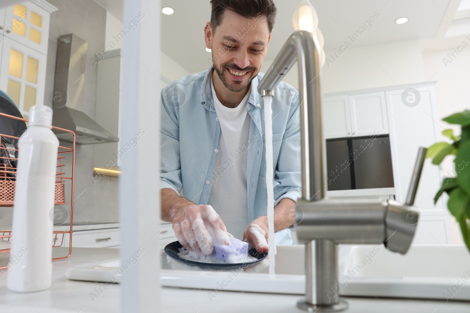 Photo of Man washing plate above sink in kitchen, view from outside