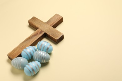 Wooden cross and painted Easter eggs on beige background, space for text