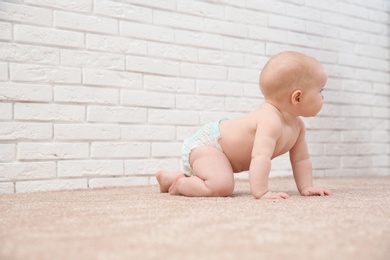 Cute little baby crawling on carpet near brick wall, space for text