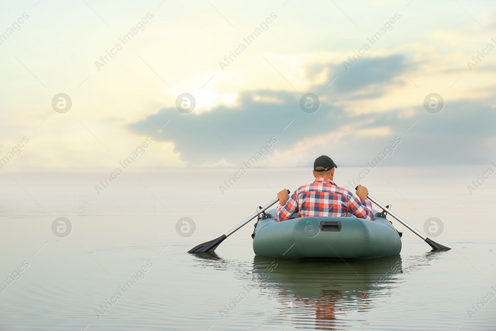 Photo of Man rowing inflatable rubber fishing boat on river, back view. Space for text