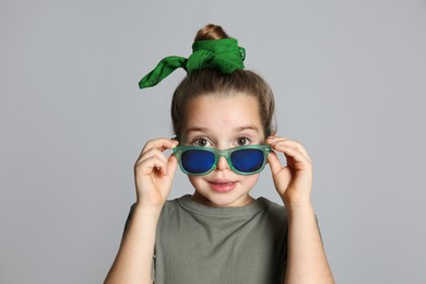 Photo of Surprised little girl with stylish bandana and sunglasses on grey background