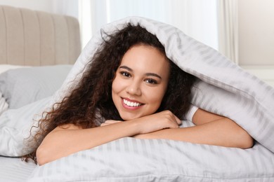 Happy beautiful African American woman lying in bed at home