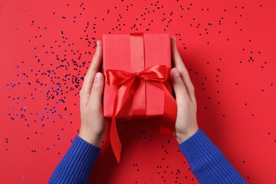 Woman with Christmas gift and confetti on red background, top view