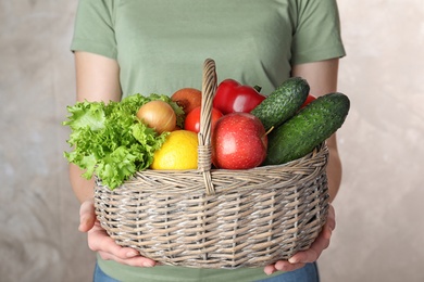 Photo of Woman holding wicker basket with ripe fruits and vegetables on color background, closeup