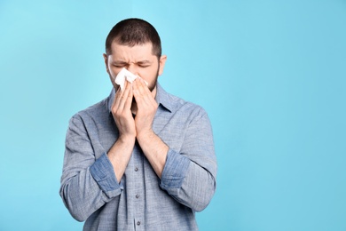 Photo of Man with tissue suffering from runny nose on light blue background. Space for text