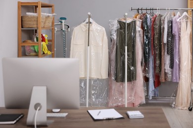 Photo of Dry-cleaning service. Hangers with different clothes in plastic bags on racks indoors