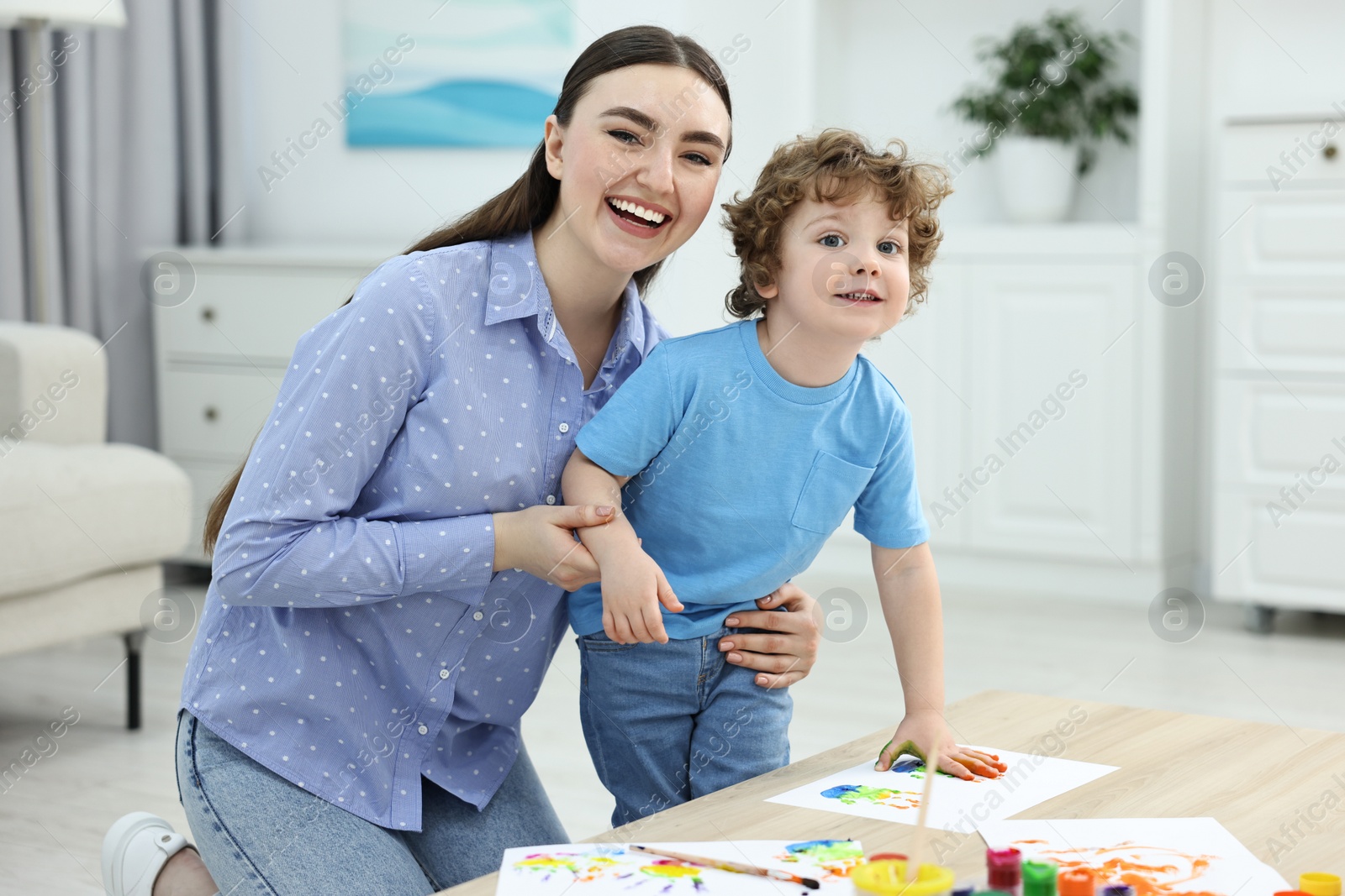 Photo of Mother and her little son painting with palms at home