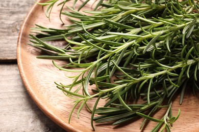 Photo of Fresh rosemary sprigs on wooden plate, closeup